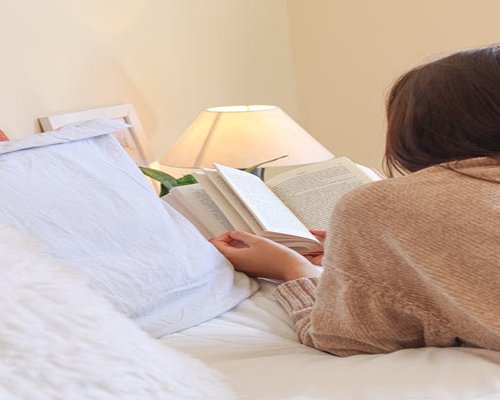 Person reading a book in bed with warm lamp light
